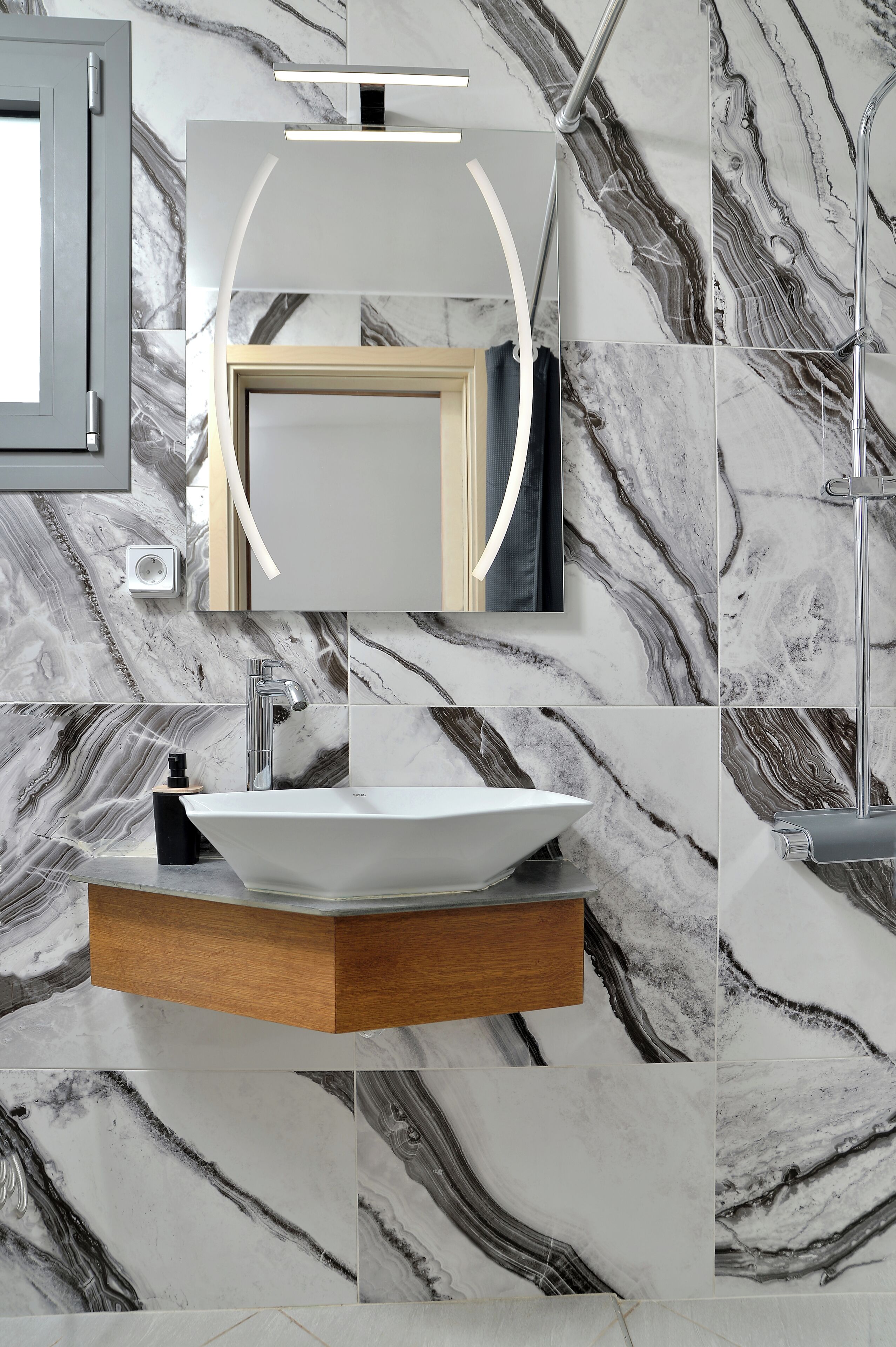 Une salle de bain avec un pare-chocs en marbre, un lavabo sur colonne, un meuble-lavabo en bois et un miroir moderne.