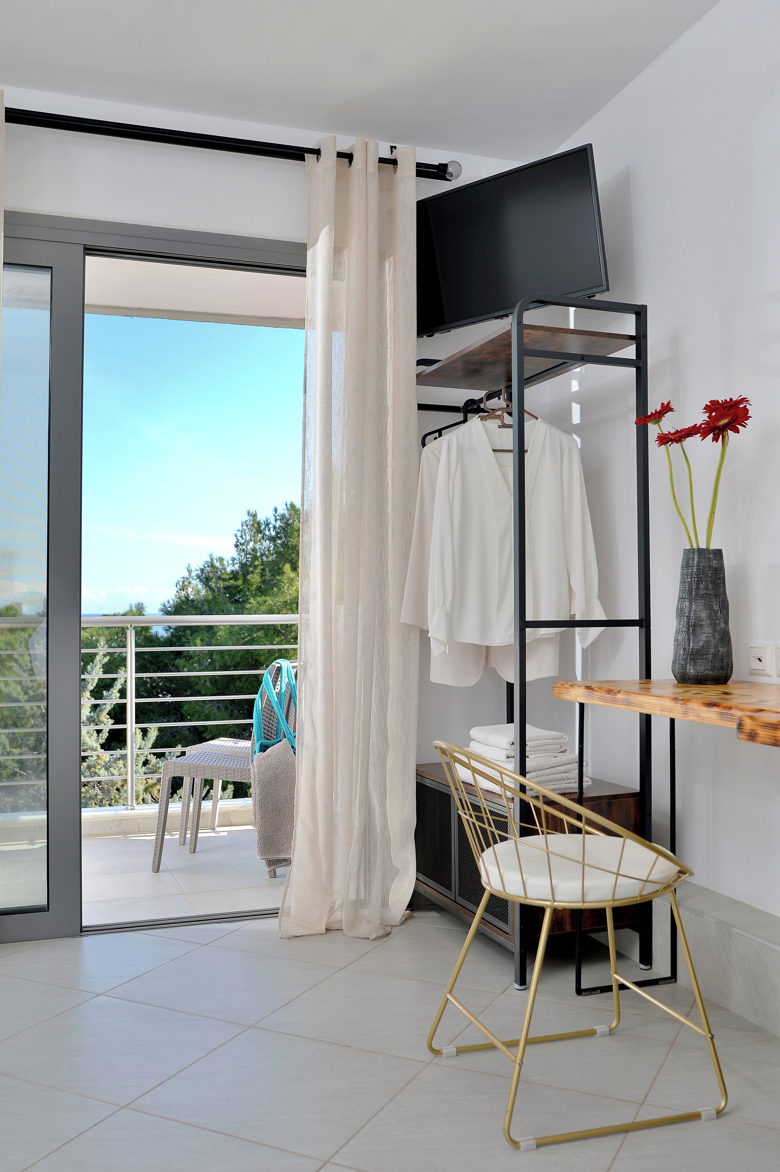 Een moderne kamer met balkon, een aan de muur bevestigde televisie, een stoel, een tafel en een vaas met bloemen.