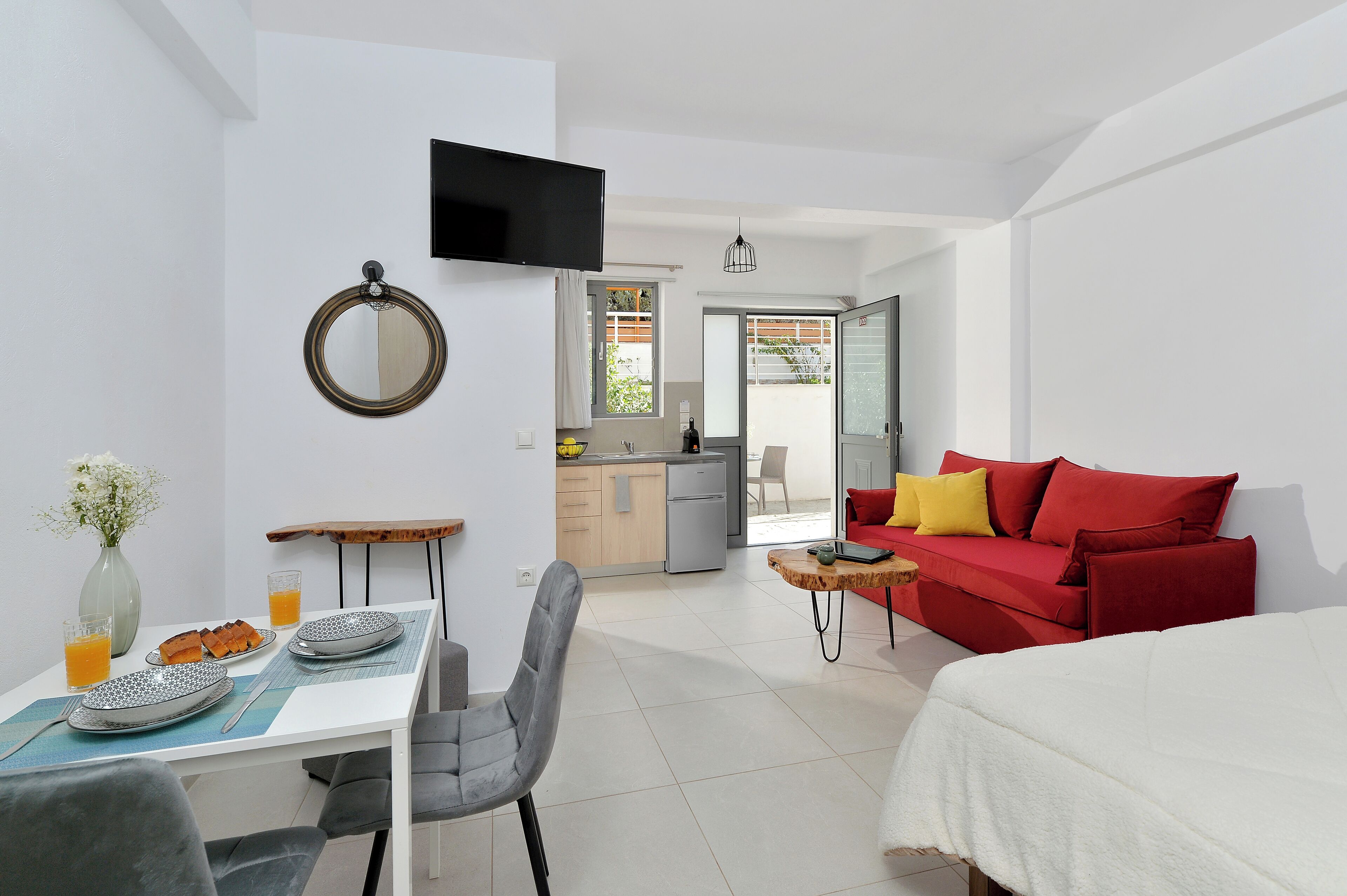 A modern room with a dining table, a red sofa, a bed, and a kitchen area.