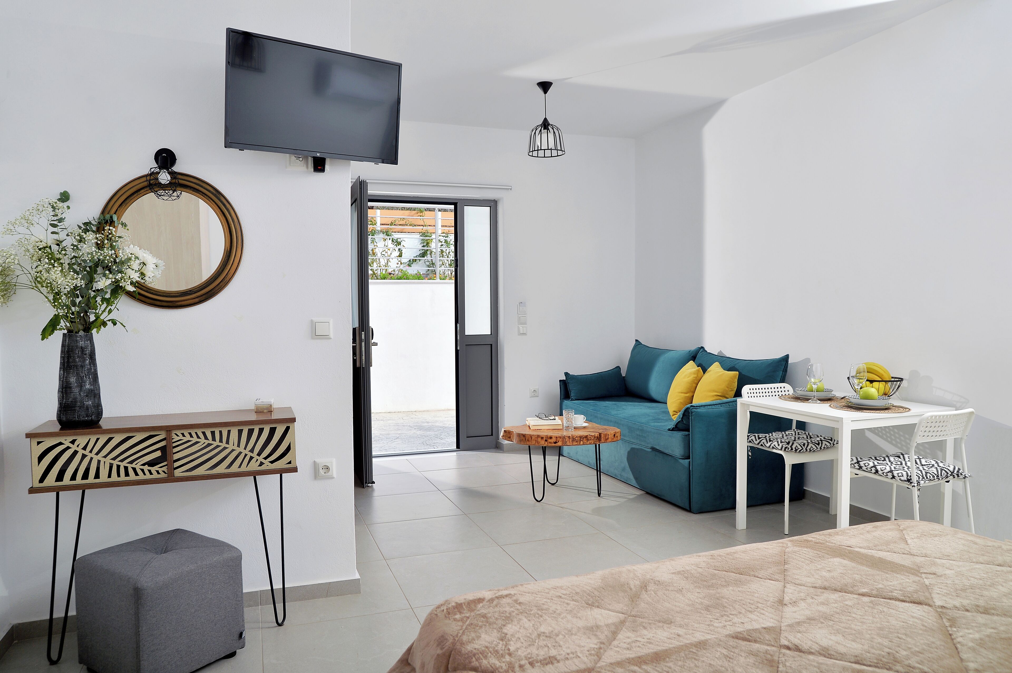 Uma sala de estar moderna com um sofá, uma mesinha, uma televisão e um espelho decorativo.