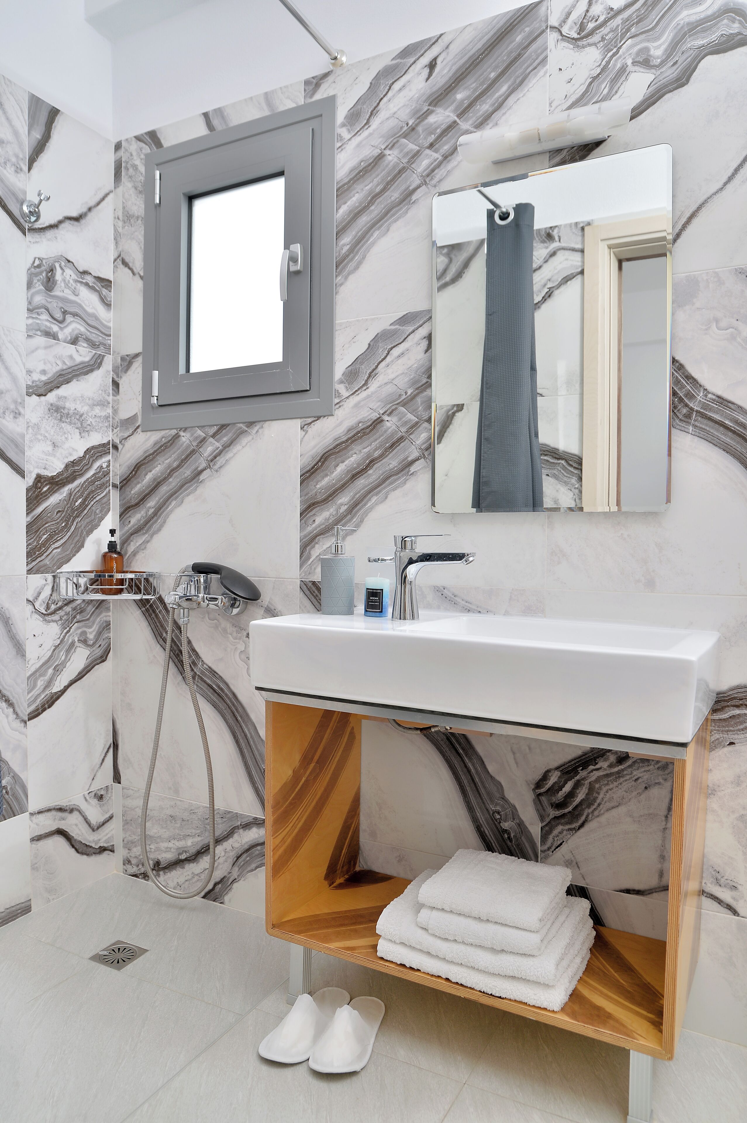 Une salle de bain avec un mur en marbre, un lavabo, un miroir, une douche et un porte-serviettes.