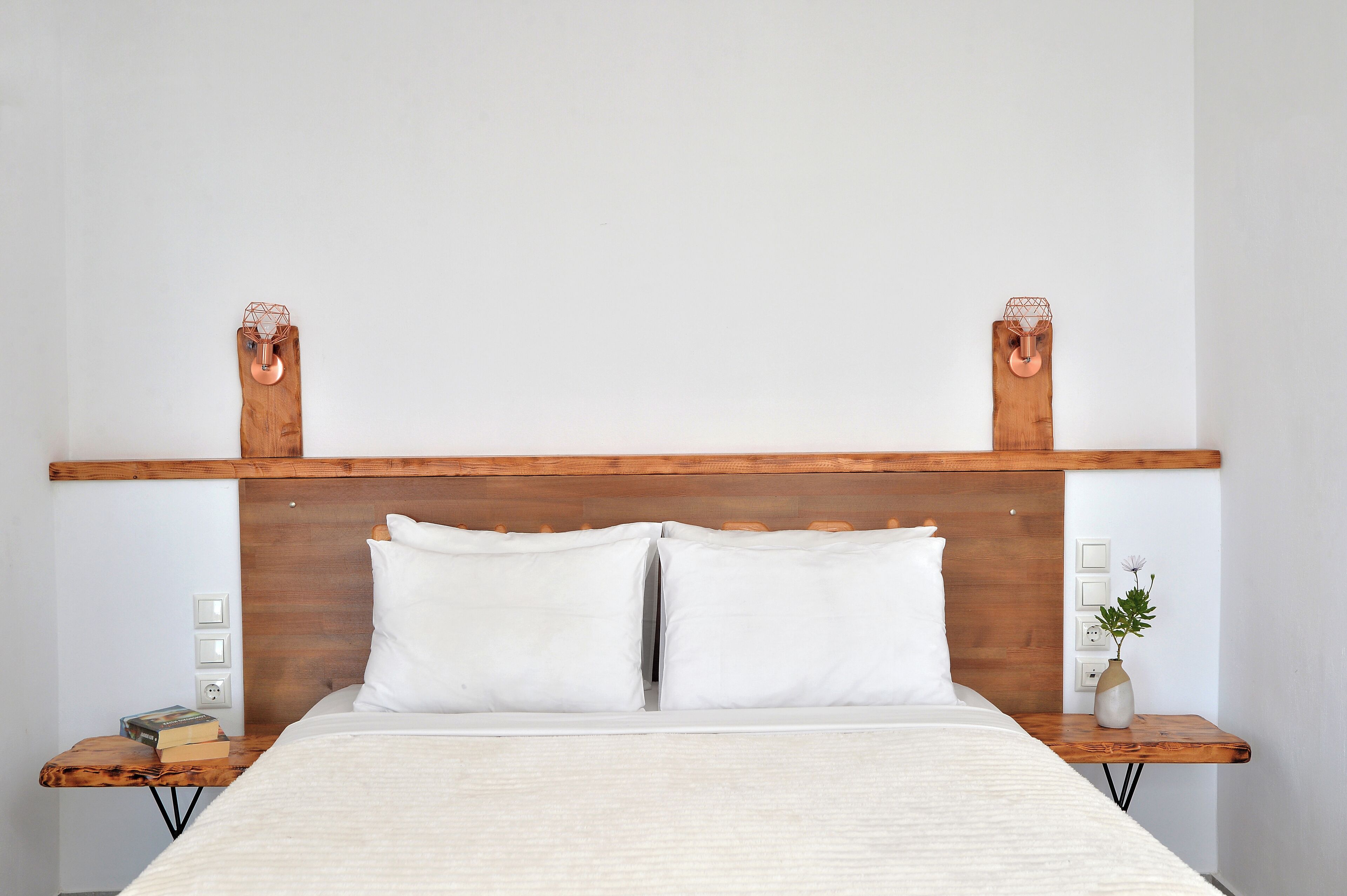A neatly made bed with white linens, a wooden headboard, and a bedside table with a vase and a book.