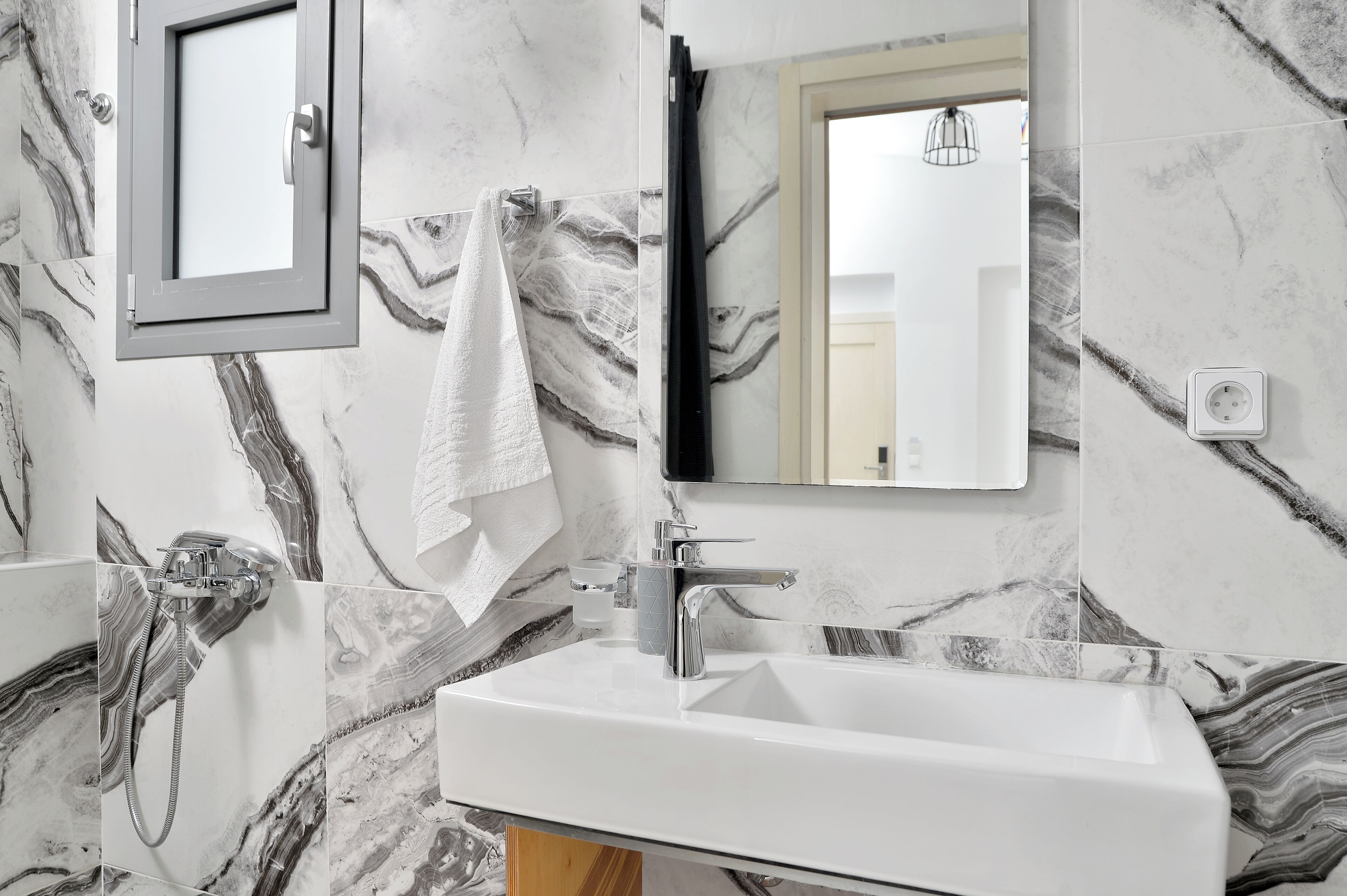 A bathroom with a marble backsplash, a white sink, a towel hanging on the wall, and a mirror.