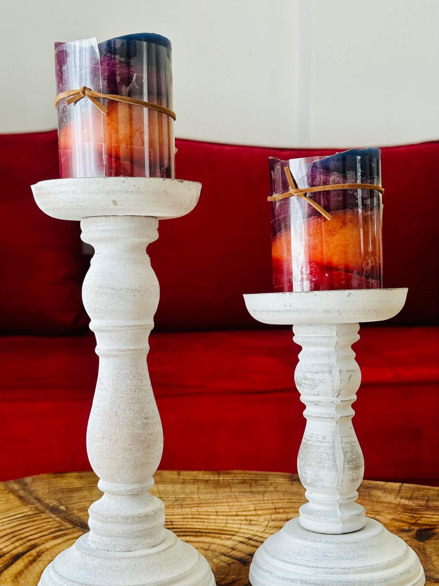 Two white candle holders with transparent glass candles on a round wooden table.