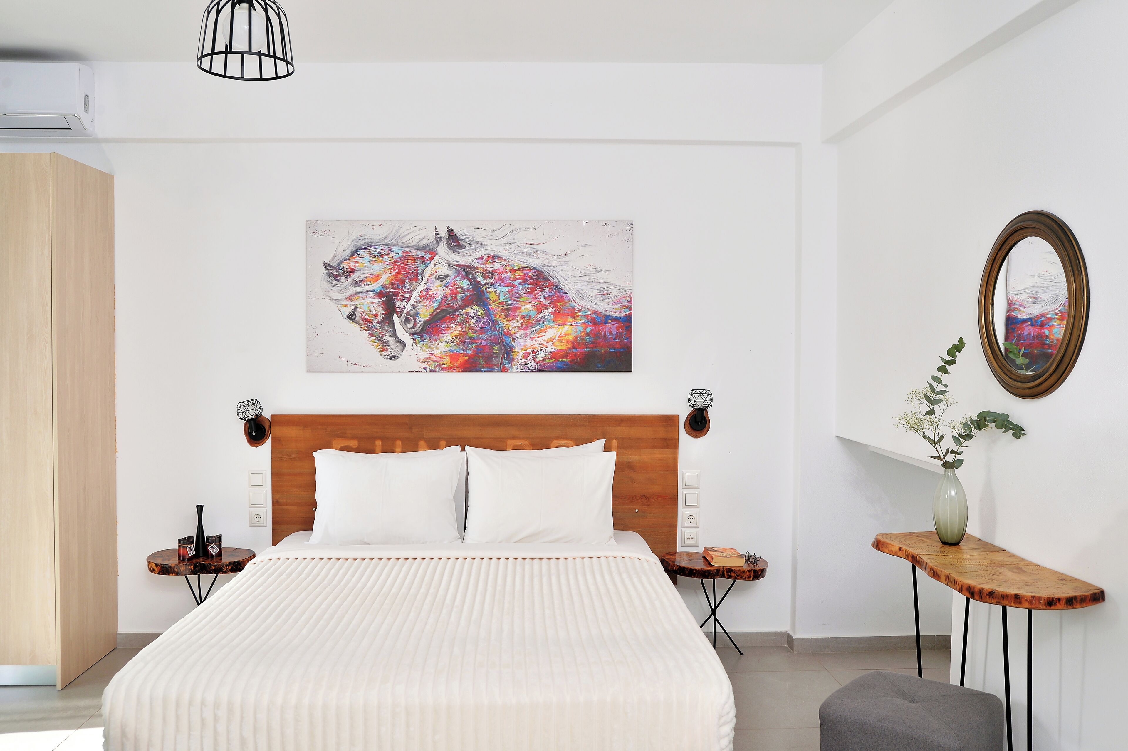 A modern bedroom with a large bed, a wooden headboard, a side table with a vase, and a painting of a horse on the wall.