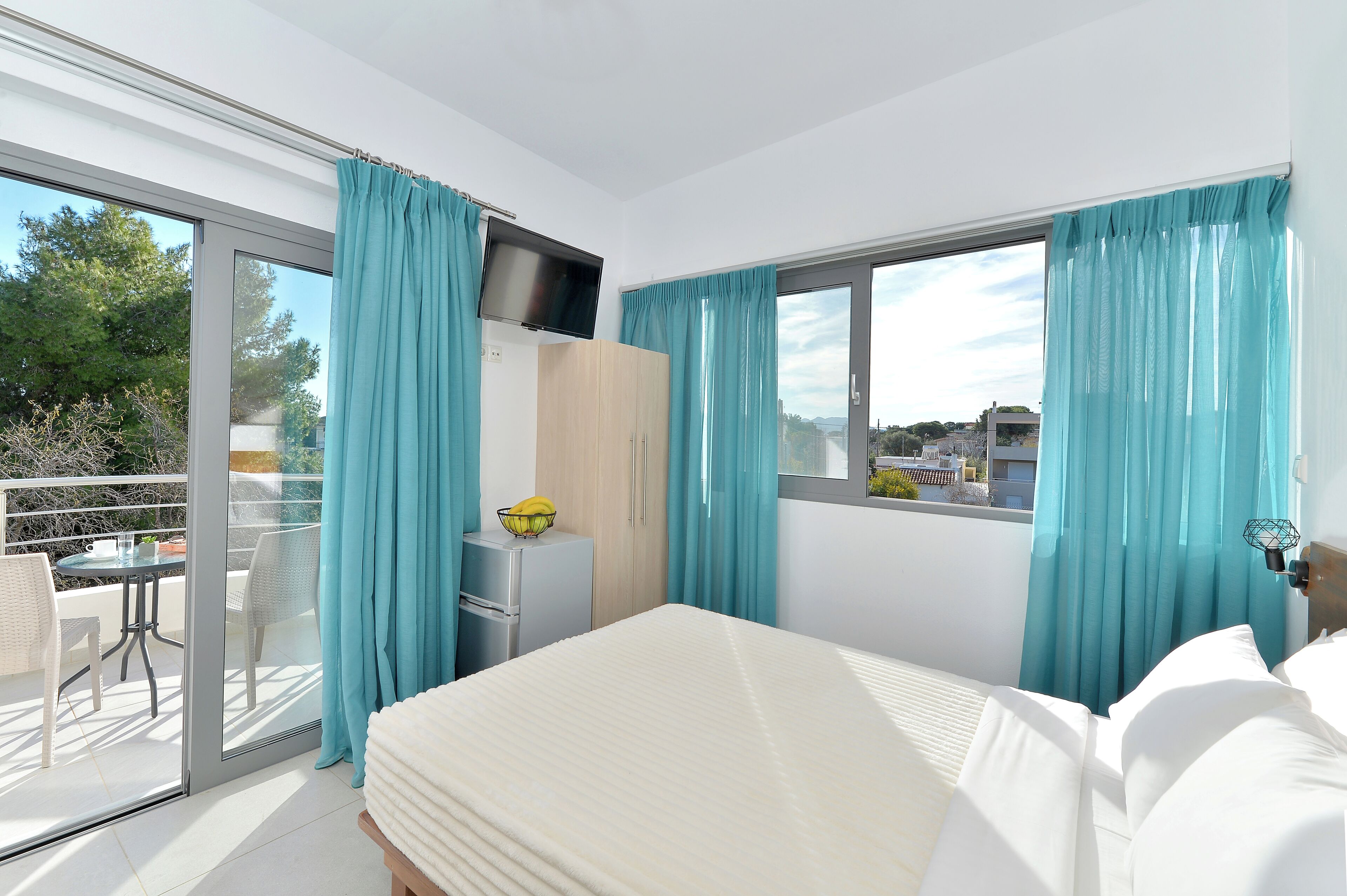 Un dormitorio con cama, televisor, armario y balcón con mesa y sillas.