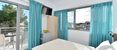 Un dormitorio con cama, televisor, armario y balcón con mesa y sillas.