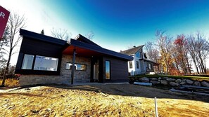 A modern two-story house with a stone foundation, large windows, and a sloped roof.