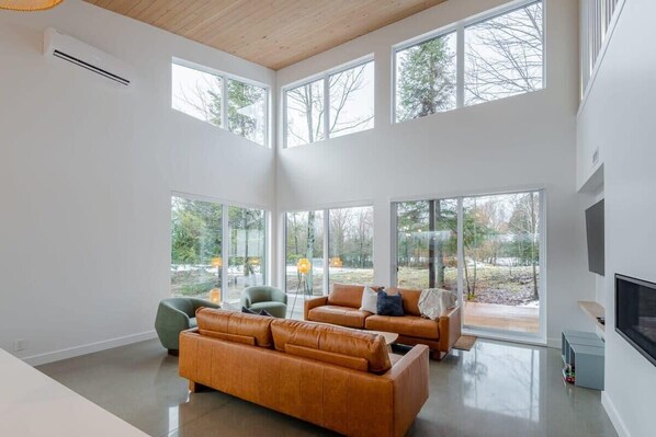 A spacious living room with large windows, a modern sofa set, and a flat-screen TV.