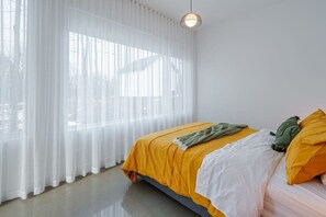 A bedroom with a bed, white curtains, and a hanging light fixture.