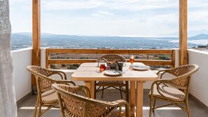 A wooden table and wicker chairs on a balcony with a view of a city and mountains. - Horizon Villa in Naxos Skyline (Naxos)