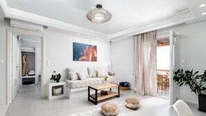 A modern living room with a sofa, coffee table, and ottomans, a ceiling light, and a view to the outside. - Horizon Villa in Naxos Skyline (Naxos)