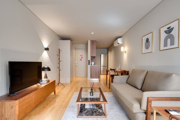 Un salon moderne avec un téléviseur à écran plat, une console en bois, une table basse en verre et un canapé beige.