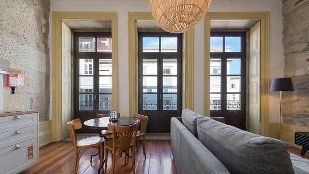 Ein gemütliches Zimmer mit Esstisch, Stühlen, einer Couch und einem großen Fenster mit Blick auf Gebäude.