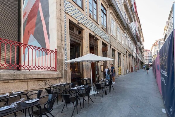Un café en plein air avec des tables et des chaises, une clôture rouge et un bâtiment orné de carreaux décoratifs et doté de fenêtres.