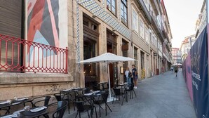 An outdoor café with tables and chairs, a red fence, and a building with patterned tiles and windows. - Mercado Apartments #3T by DA'HOME (Porto)