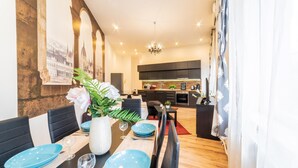 Un comedor moderno con una larga mesa dispuesta para cuatro, un florero con flores y una vista de una cocina y comedor al fondo.
