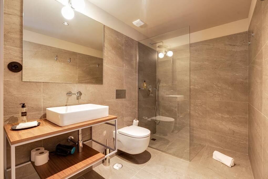 A modern bathroom with a large mirror, a white sink, a toilet, and a glass-enclosed shower area.