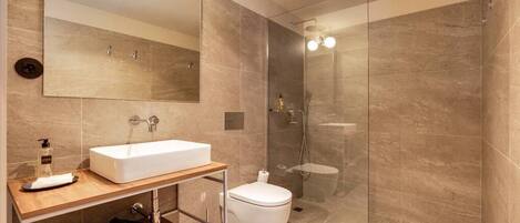A modern bathroom with a large mirror, a white sink, a toilet, and a glass-enclosed shower area.