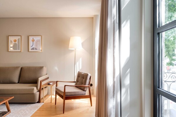 A modern living room with a sofa, a chair, a floor lamp, and two framed artworks on the wall.