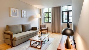 A modern living room with a sofa, armchair, coffee table, lamp, and large windows with curtains.