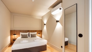 A modern hotel room with a large bed, wooden headboard, bedside lamps, and a large mirror.