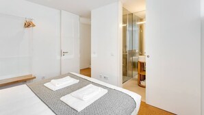 Una camera d'hotel moderna con un letto grande, un piccolo angolo relax e un bagno con pareti in vetro.