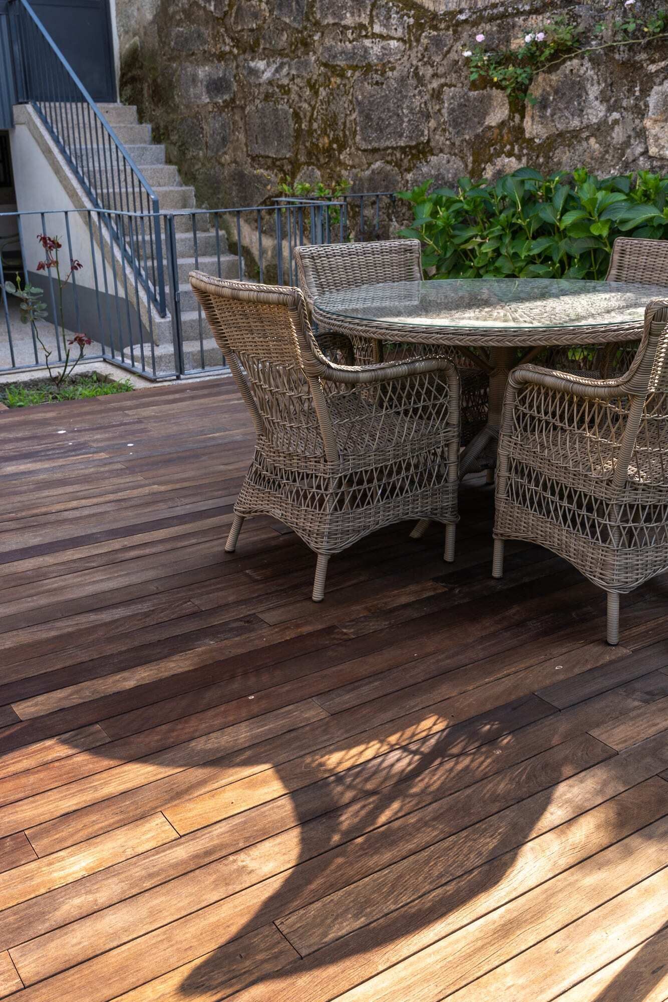 A wooden deck with wicker furniture and a glass table.