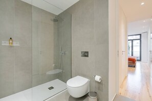 A modern bathroom with a glass shower enclosure, a white toilet, and a small trash bin. - Alma da Casa by DA'Home #1D (Porto)