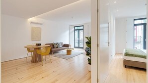 A modern living room with a wooden floor, a round dining table with yellow chairs, a sofa, and a bed with a green blanket. - Alma da Casa by DA'Home #2E (Porto)