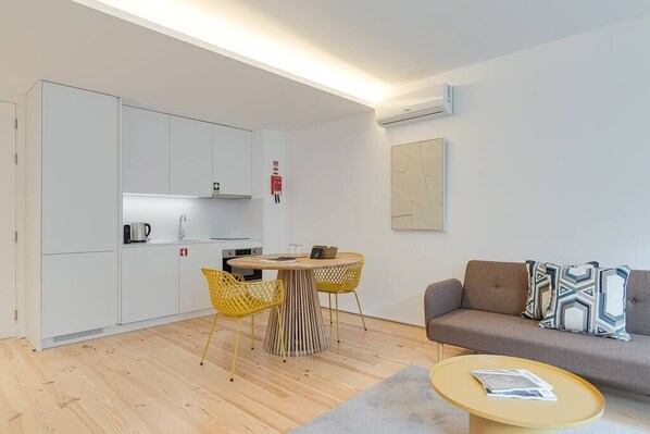 A compact living space with a kitchenette, a dining area with yellow chairs, a sofa with patterned cushions, and a small coffee table.