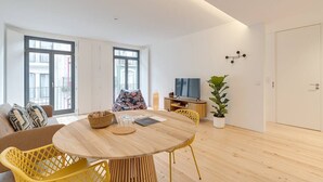 A modern living room with a round wooden table, yellow chairs, a sofa, a TV, and a potted plant. - Alma da Casa by DA'Home #2E (Porto)