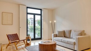 A modern living room with a sofa, a wooden coffee table, a chair, and a large window with a view of buildings and greenery. - Alma da Casa by DA'Home #3D (Porto)