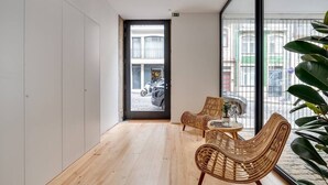 A modern interior with a wooden floor, two wicker chairs, a small round table, and a large window with a view of the street outside. - Alma da Casa by DA'Home #3D (Porto)