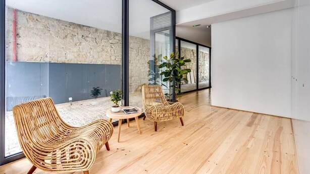 A spacious room with large windows, a stone wall, and two wicker chairs with a small table. - Alma da Casa by DA'Home #3D (Porto)