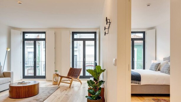 Eine moderne Wohnung mit großem Fenster, Holzboden, einer Couch, einem Couchtisch, einem Sessel und einem Bett.