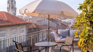 A balcony with outdoor furniture, a large umbrella, and a view of a historic building with a clock tower. - Alma da Casa by DA'Home #4E (Porto)