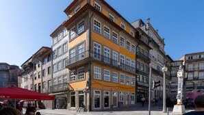 Ein mehrstöckiges Gebäude mit gelber Fassade und mehreren Balkonen, vor dem sich eine Fußgängerstraße erstreckt.