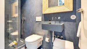 Ein modernes Badezimmer mit Duschkabine aus Glas, einer weißen Toilette, einem grauen Waschbecken und einem spiegel mit Holzrahmen darüber. Ein Handtuchhalter ist ebenfalls vorhanden.