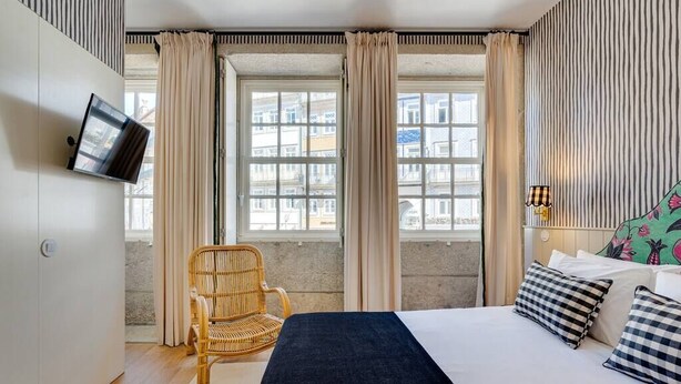 Ein Hotelzimmer mit einem Bett, einem Sessel, einem an der Wand befestigten Fernseher und einem Fenster mit Vorhängen.