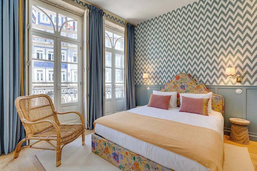 A bedroom with a bed, a chair, and a view of buildings through the window.