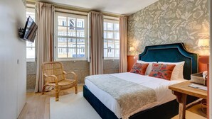 A hotel room with a large bed, a chair, a wooden nightstand, and a TV mounted on the wall.