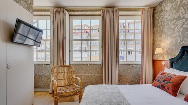 A hotel room with a bed, a chair, a TV, and a window with curtains.
