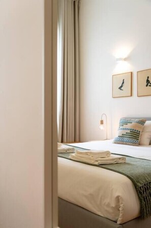 Une chambre d’hôtel avec un lit, une table de chevet, une lampe et une fenêtre avec des rideaux.