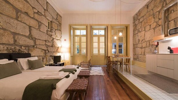 Ein Zimmer mit zwei Betten, einem kleinen Tisch, einer Bank und einer Küchenzeile.