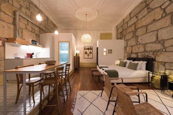 A compact living space with a kitchenette, dining area, and a bed with a stone wall backdrop.