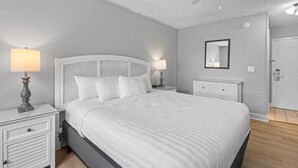 Ein Schlafzimmer mit einem Bett, zwei Nachttischen mit Lampen, einem Deckenventilator, einer Tür und einem an der Wand befestigten Spiegel.