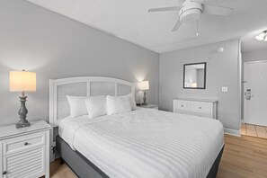 Ein Schlafzimmer mit einem Bett, zwei Nachttischen mit Lampen, einem Deckenventilator, einer Tür und einem an der Wand befestigten Spiegel.