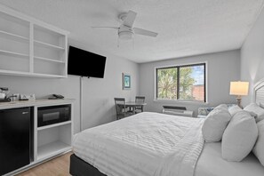 Habitación de hotel con cama, escritorio con microondas, televisión y ventana con persianas.