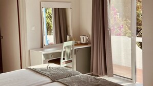 Una camera da letto con un letto, una scrivania, una sedia, uno specchio e una porta-vetro scorrevole su un balcone.